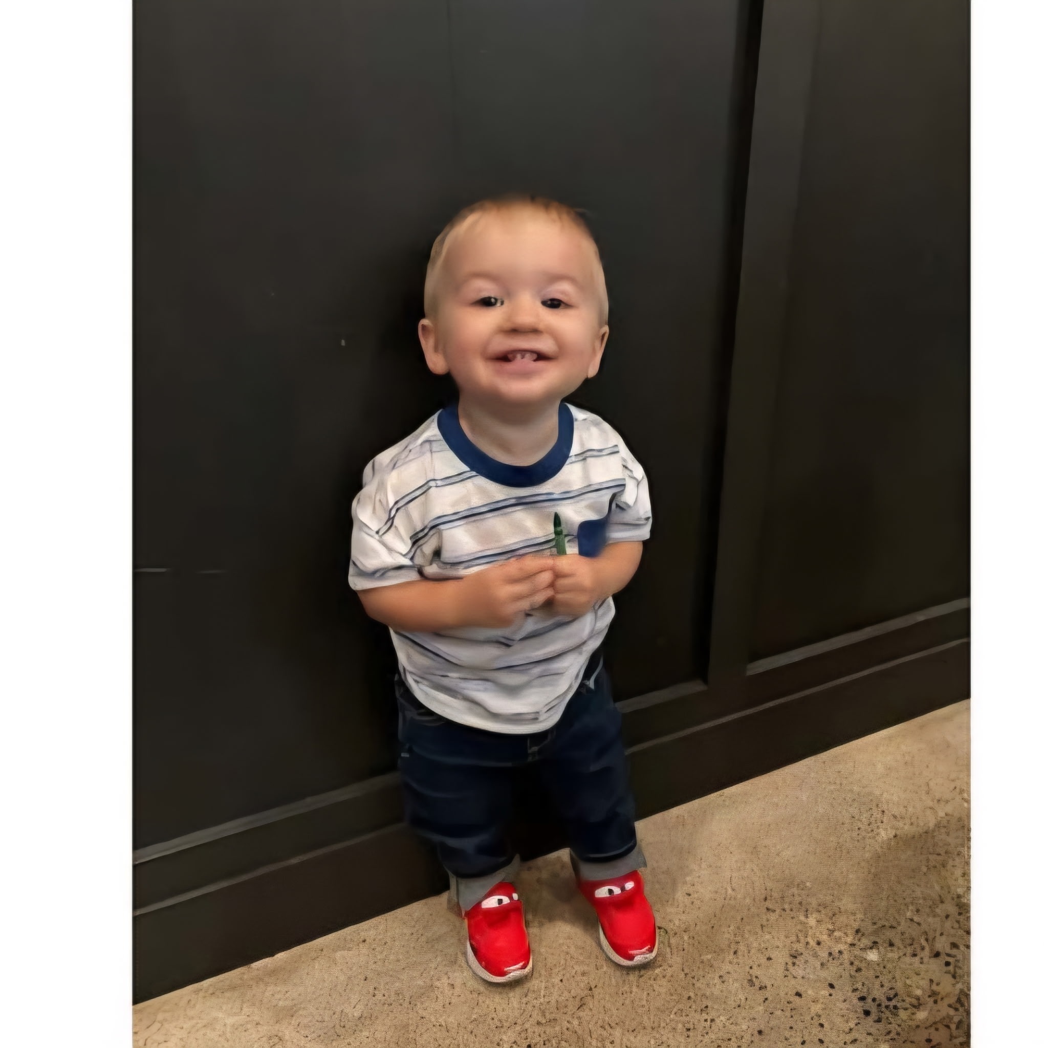 Tucker Adamek smiling and holding a crayon, wearing his red Cars shoes